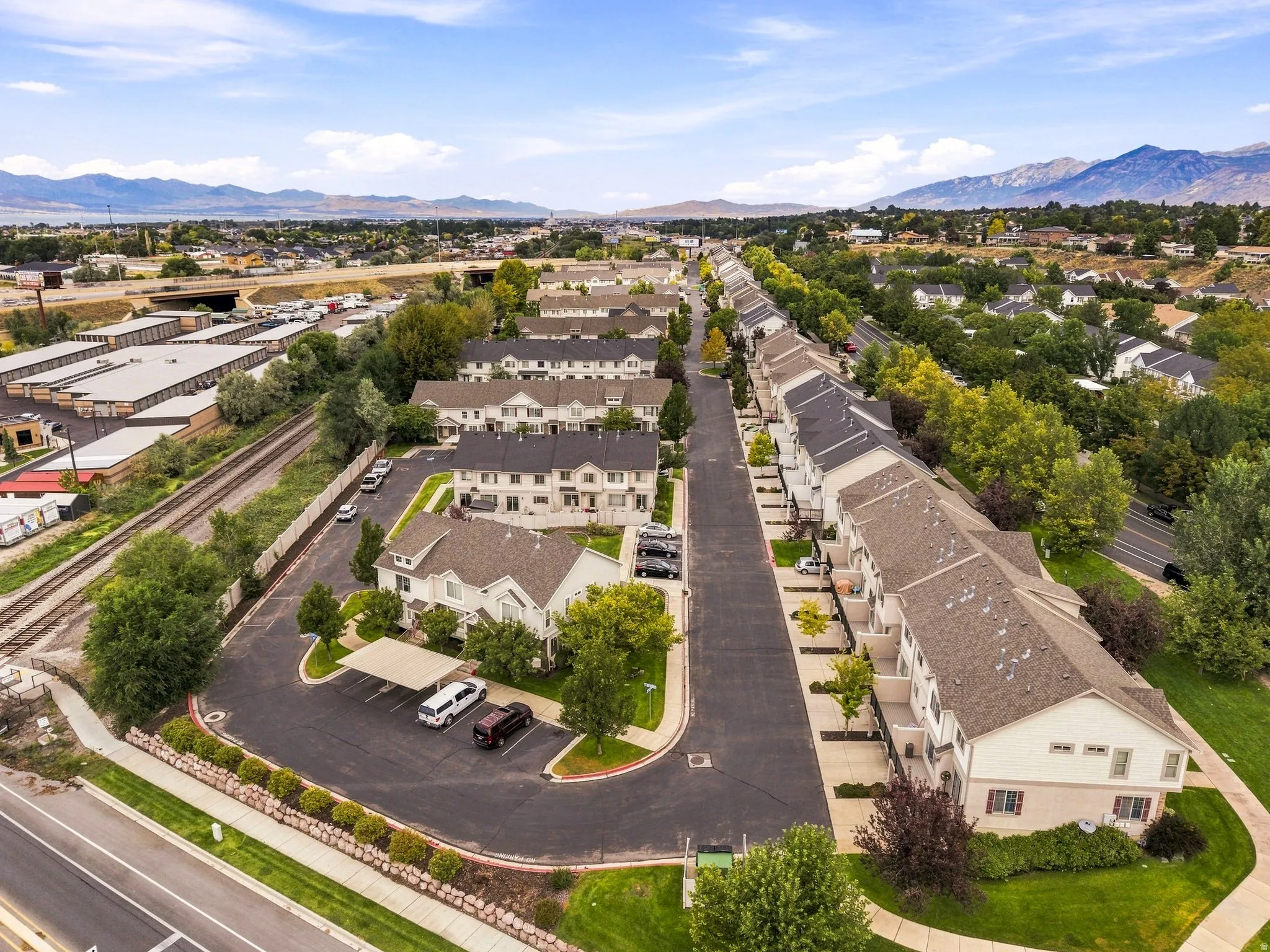 Residential community featuring multi-story townhomes, paved roadways, mature trees, and covered parking