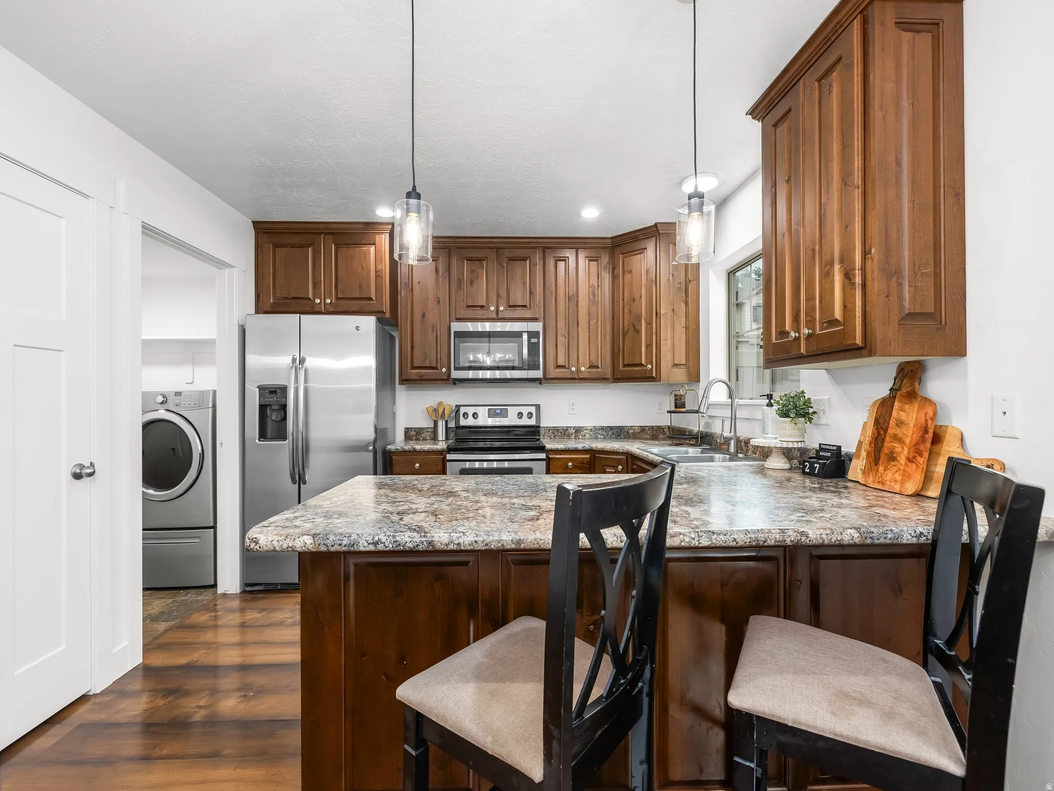 Kitchen featuring wood-finish cabinetry, stainless steel appliances, a multi-tone countertop, and pendant lighting
