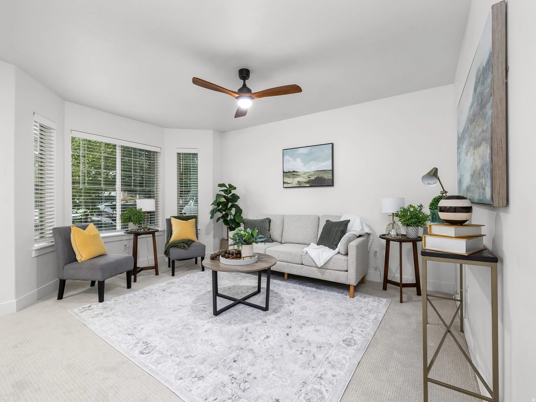 Bay window with window blinds, neutral wall paint, ceiling fan with light fixture, and light-toned carpet flooring