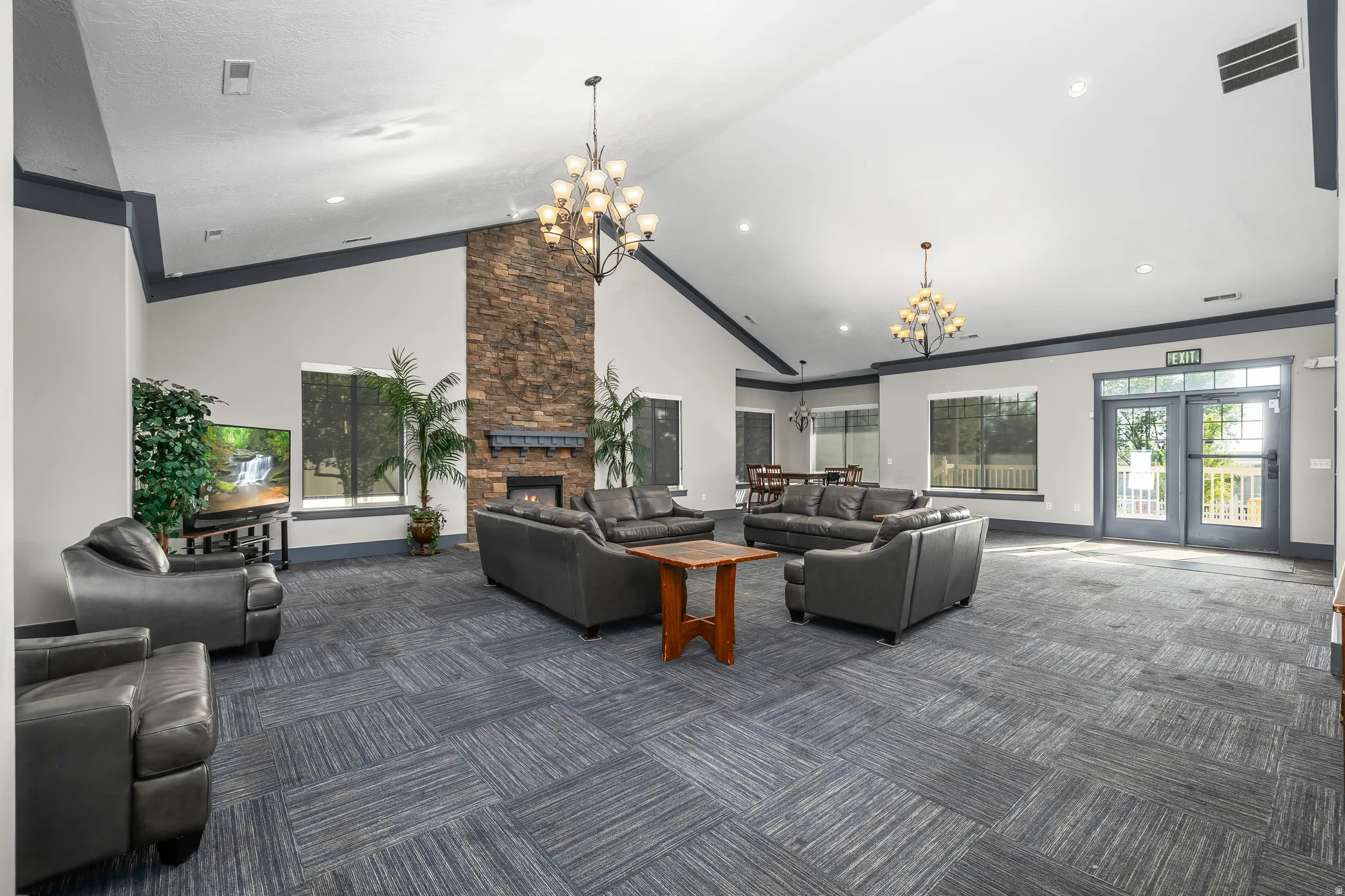 Vaulted ceilings with exposed beams, stone-clad fireplace with mantel, large windows, French doors with full glass panels, and patterned carpet flooring