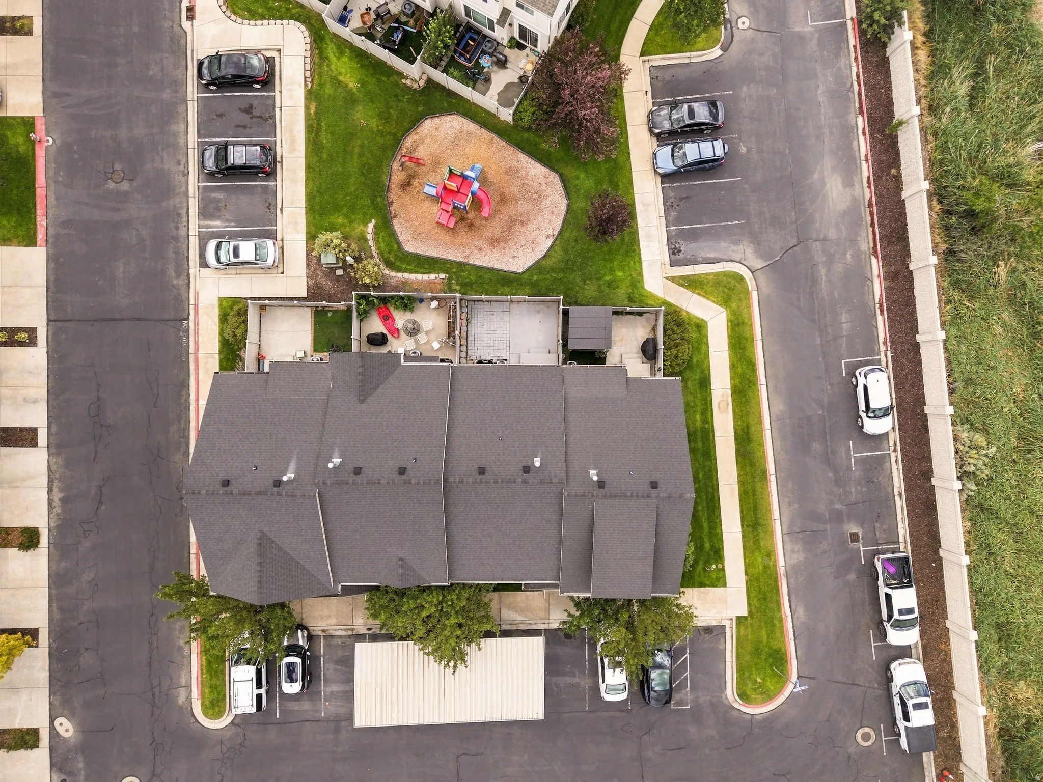Gable roofline with multiple vent stacks, covered outdoor patios, paved parking areas, and mature trees