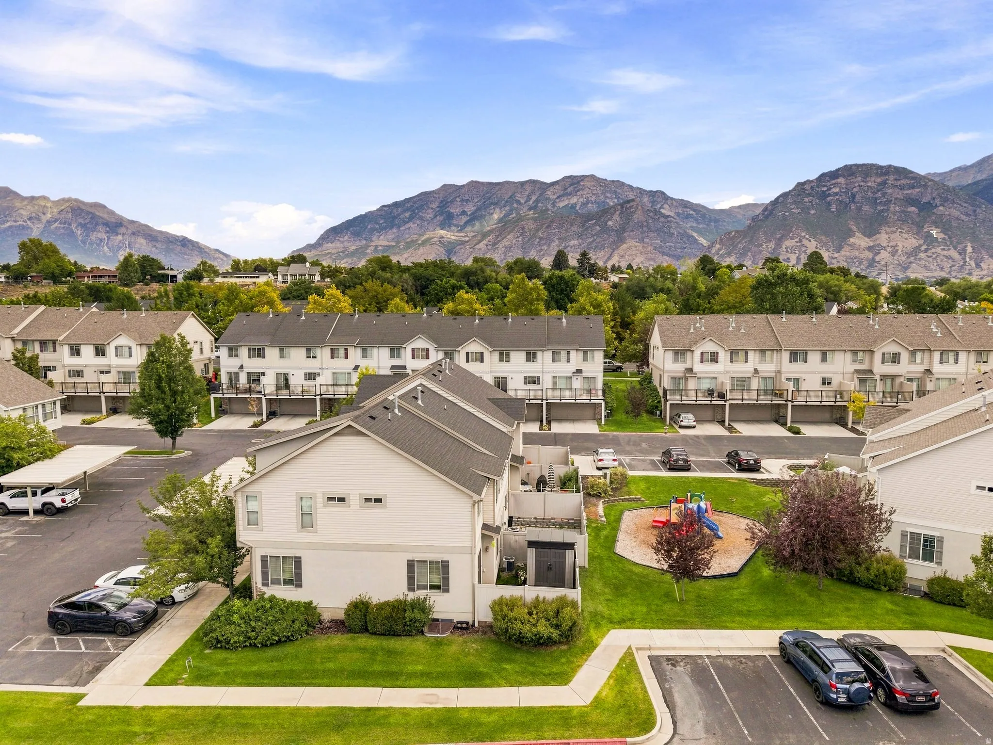 Mountain backdrop, residential community, multiple two-story townhomes, manicured green spaces, and a dedicated play area