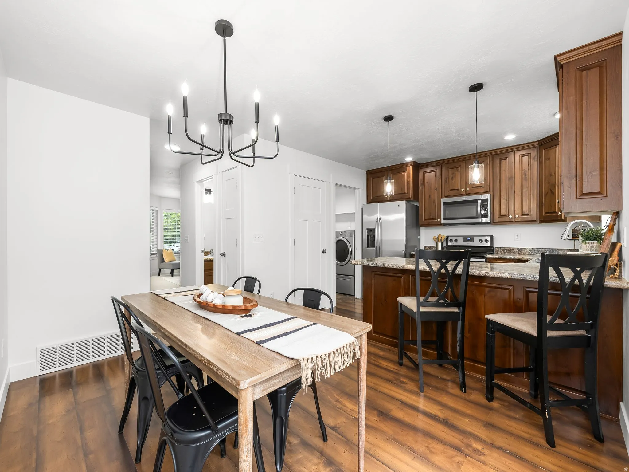 Wood-finish flooring, dark wood cabinetry, stainless steel appliances, speckled countertops, and a modern black chandelier
