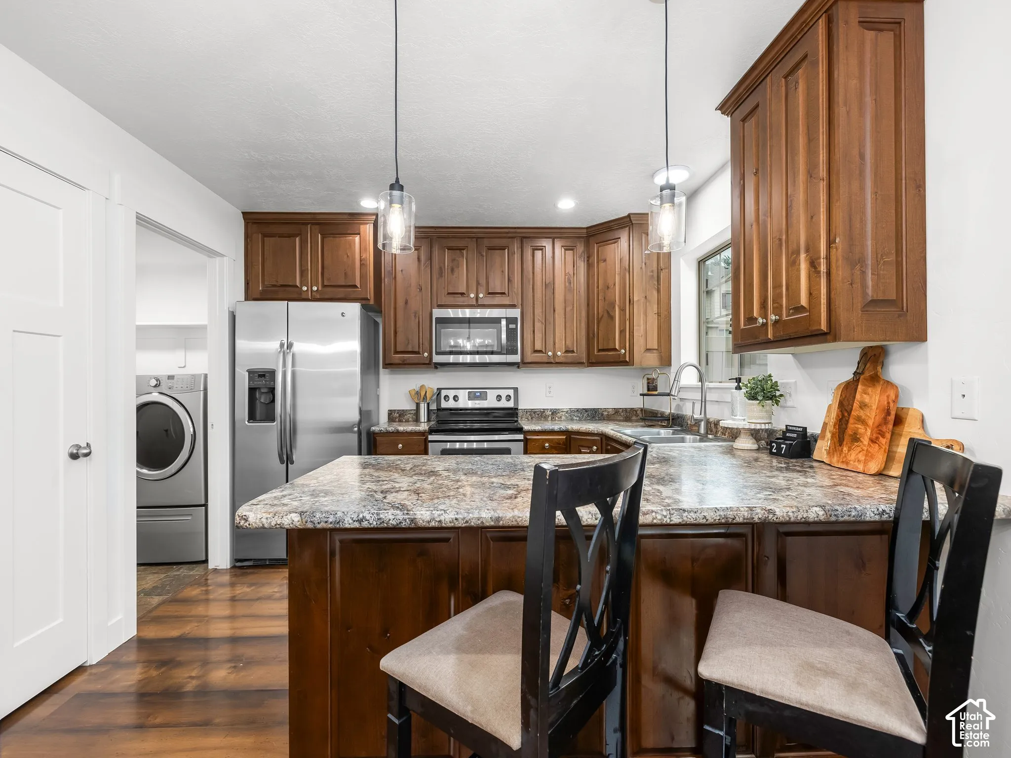 Kitchen featuring wood-finish cabinetry, stainless steel appliances, a multi-tone countertop, and pendant lighting