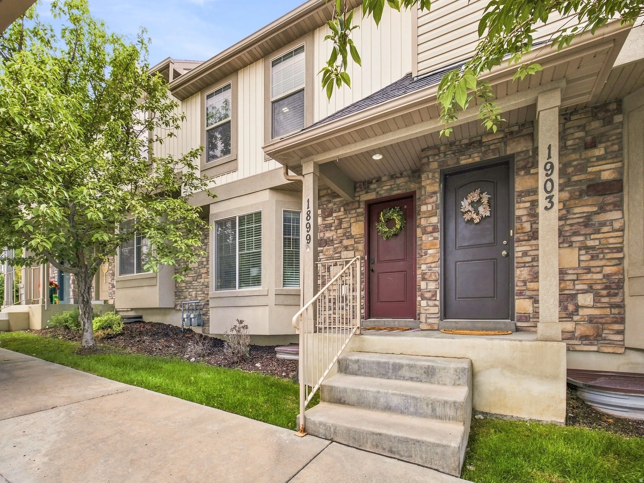 Stone veneer facade with siding accents, concrete steps with metal handrails, and a covered entry