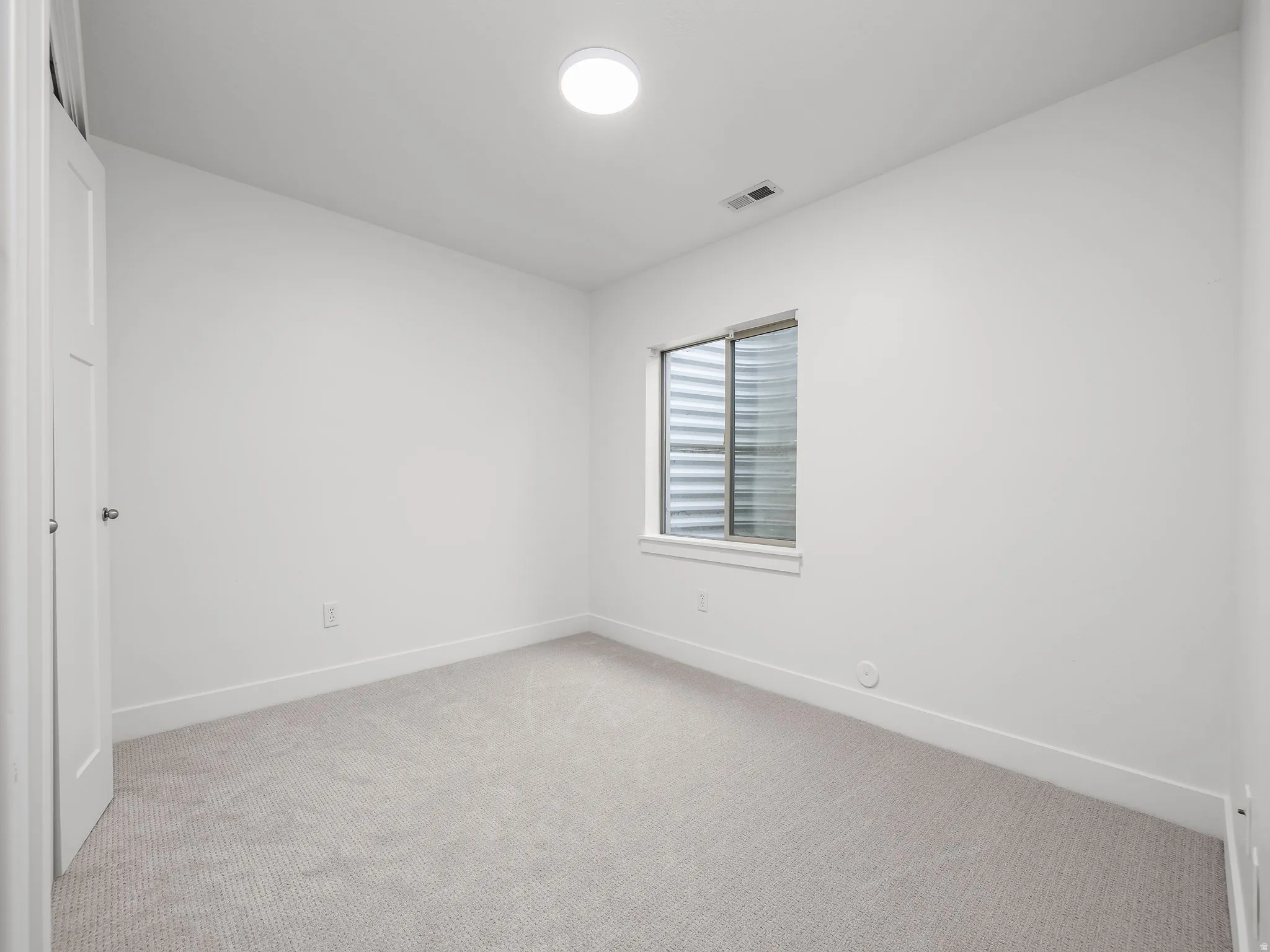 Neutral wall color, light-toned carpeting, flush-mount ceiling light, window with horizontal blinds, and white trim