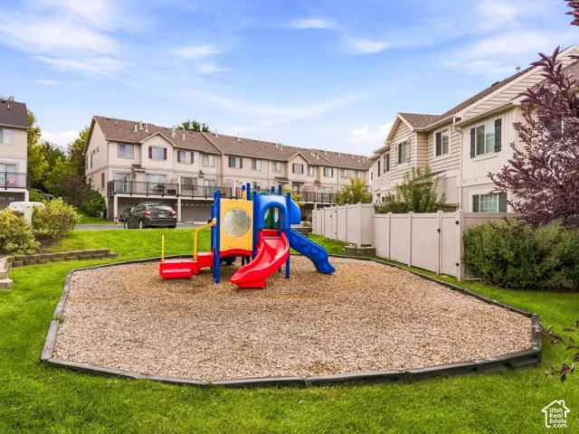 Community playground with wood chip ground cover, bordered by green lawn and a vinyl fence