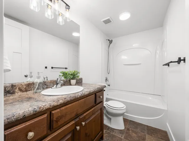 Bathroom featuring a single vanity with wood cabinetry, a granite-finish countertop, an integrated sink, a full-width mirror, and a tub/shower combination