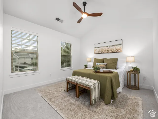Vaulted ceiling, ceiling fan with integrated lighting, two windows with blinds, light-toned carpet flooring, and white painted walls