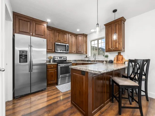 Wood-finish flooring, wood cabinetry, stainless steel appliances, granite-style countertops, and a kitchen island with pendant lighting