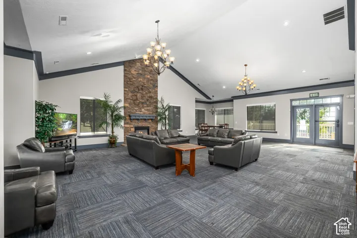 Vaulted ceilings with exposed beams, stone-clad fireplace with mantel, large windows, French doors with full glass panels, and patterned carpet flooring