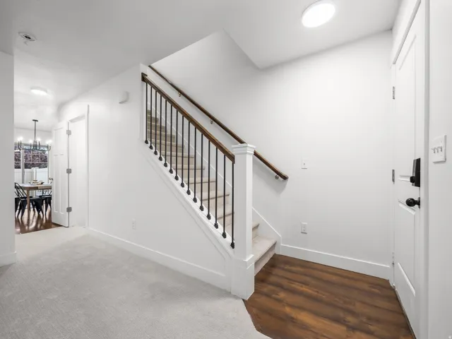 Hardwood-finish flooring at entry, carpeted staircase with wood handrail and black metal balusters, and white paneled doors