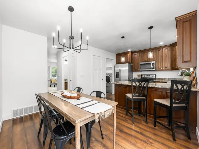 Wood-finish flooring, dark wood cabinetry, stainless steel appliances, speckled countertops, and a modern black chandelier