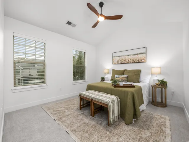 Vaulted ceiling, ceiling fan with integrated lighting, two windows with blinds, light-toned carpet flooring, and white painted walls