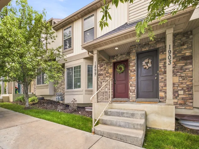 Stone veneer facade with siding accents, concrete steps with metal handrails, and a covered entry