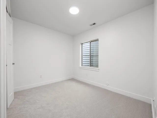 Neutral wall color, light-toned carpeting, flush-mount ceiling light, window with horizontal blinds, and white trim
