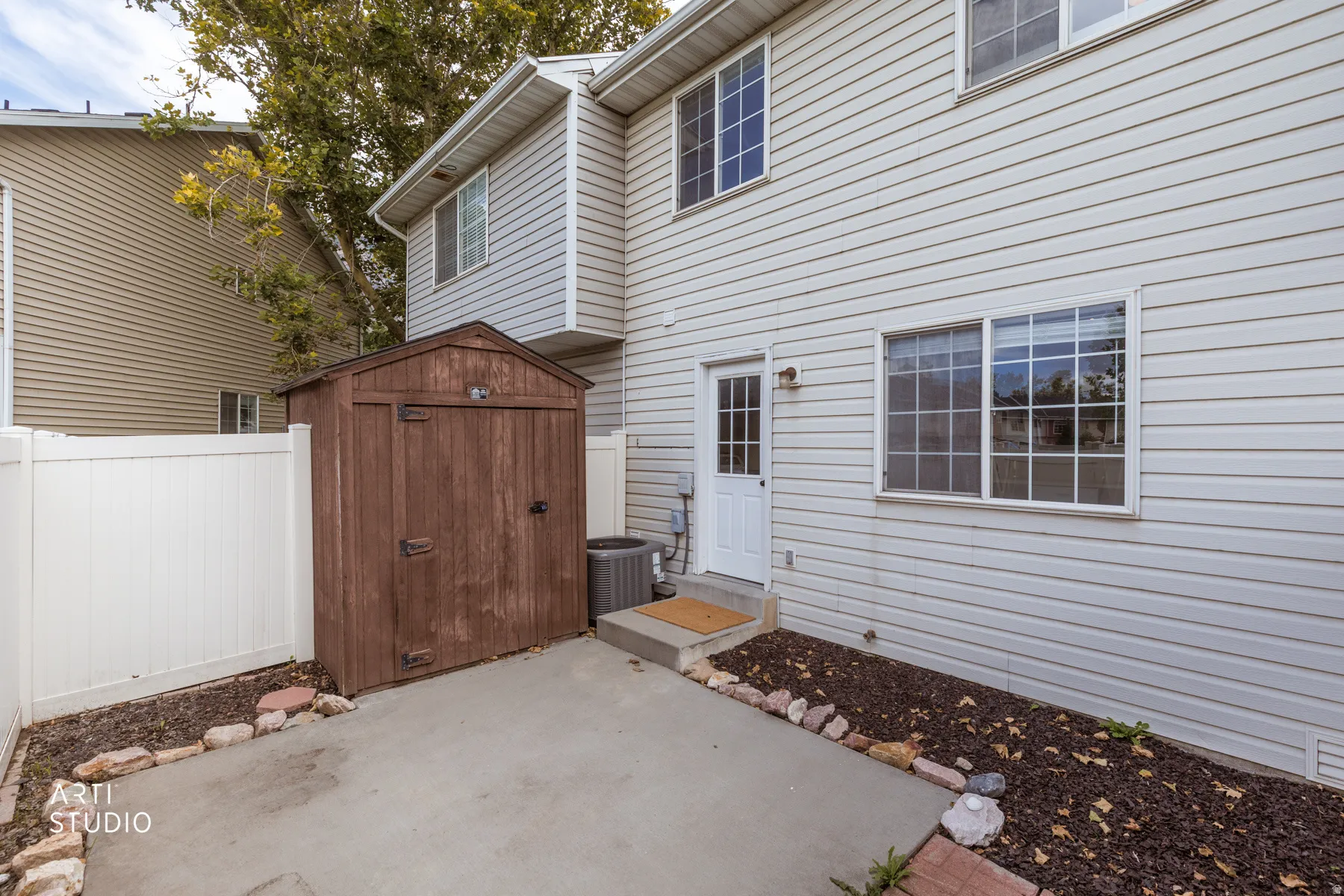 Private outdoor patio featuring a storage shed, white vinyl fencing, and a side entry door