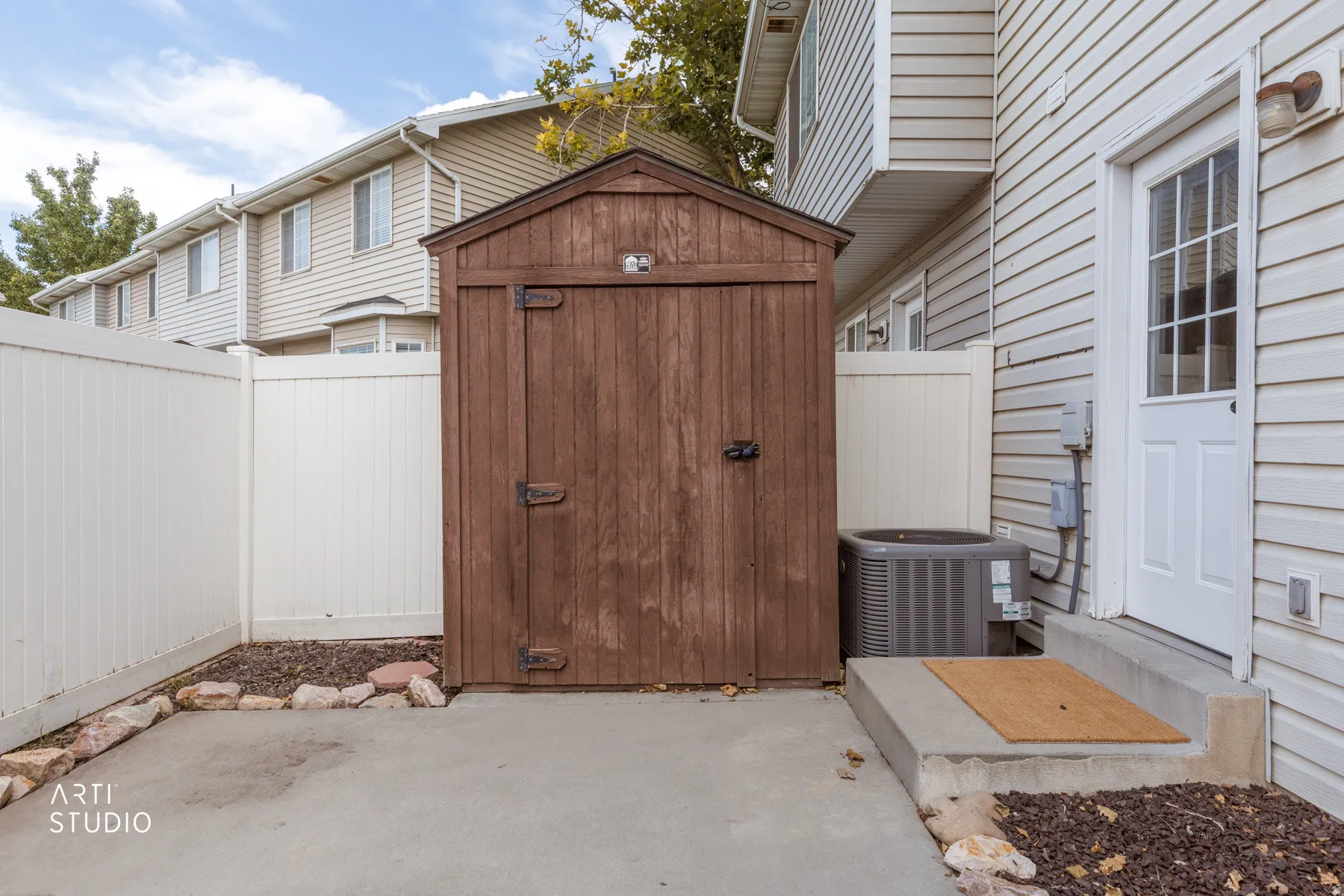 Enclosed concrete patio featuring a wooden storage shed, white vinyl fencing, and exterior access door
