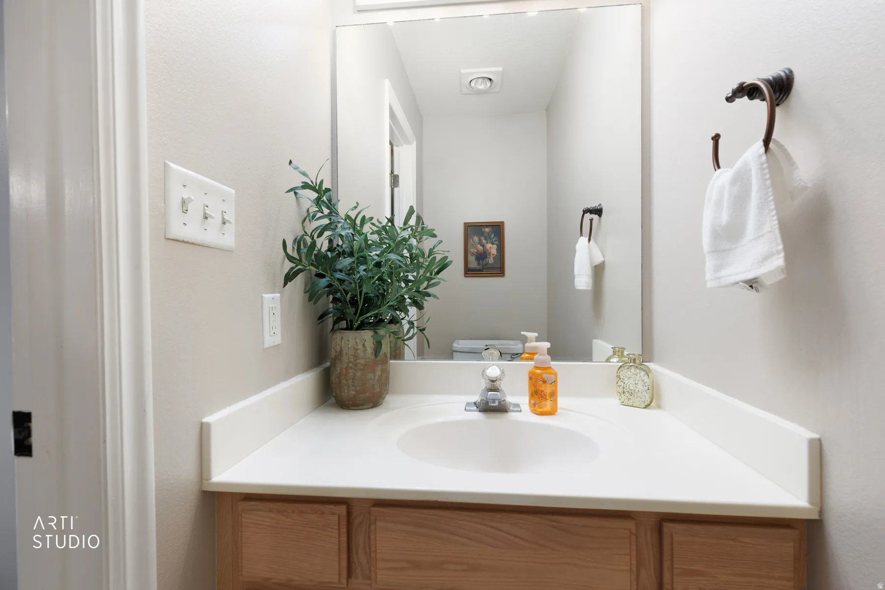 Light wood-finish vanity with a built-in sink, white countertop, and wall-mounted mirror