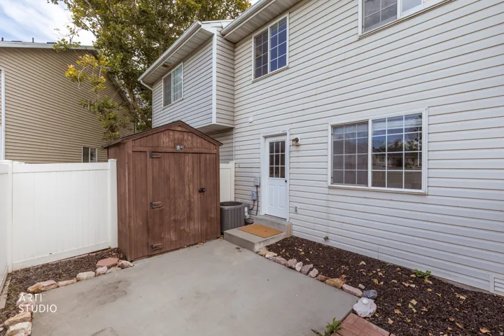 Private outdoor patio featuring a storage shed, white vinyl fencing, and a side entry door