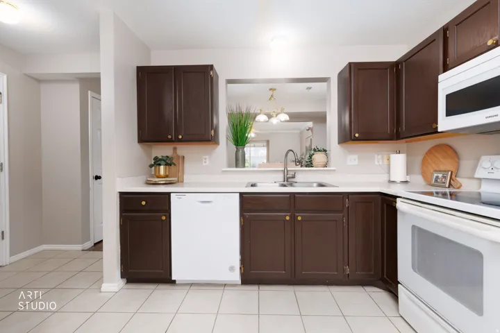 Kitchen featuring dark wood cabinetry, light countertops, stainless steel sink with a gooseneck faucet, white dishwasher, and white tile flooring