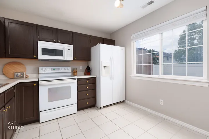 Kitchen with dark wood cabinetry, light countertops, white appliances, and tiled flooring