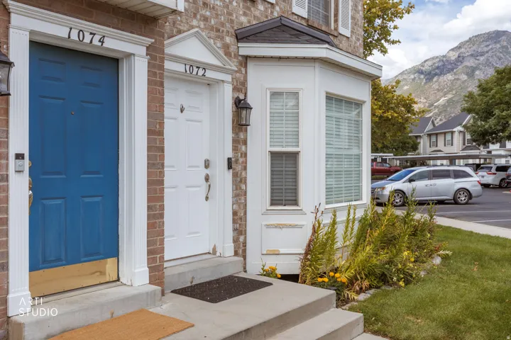 Brick exterior detailing, white bay window, manicured shrubs, concrete steps, and exterior lighting fixtures