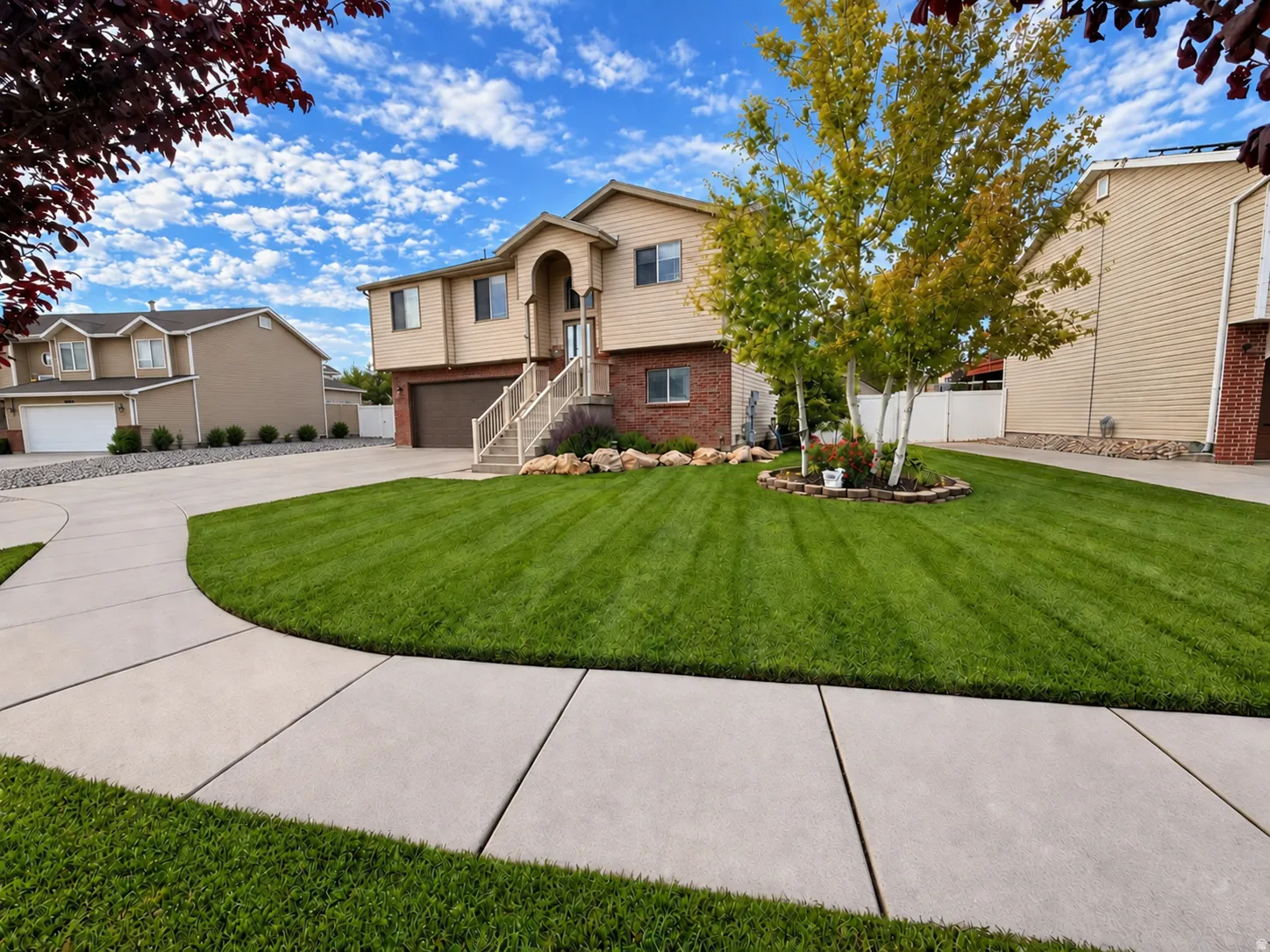 Split-level residence featuring a prominent arched entry, brick accents, a well-manicured lawn, mature trees, and a concrete driveway