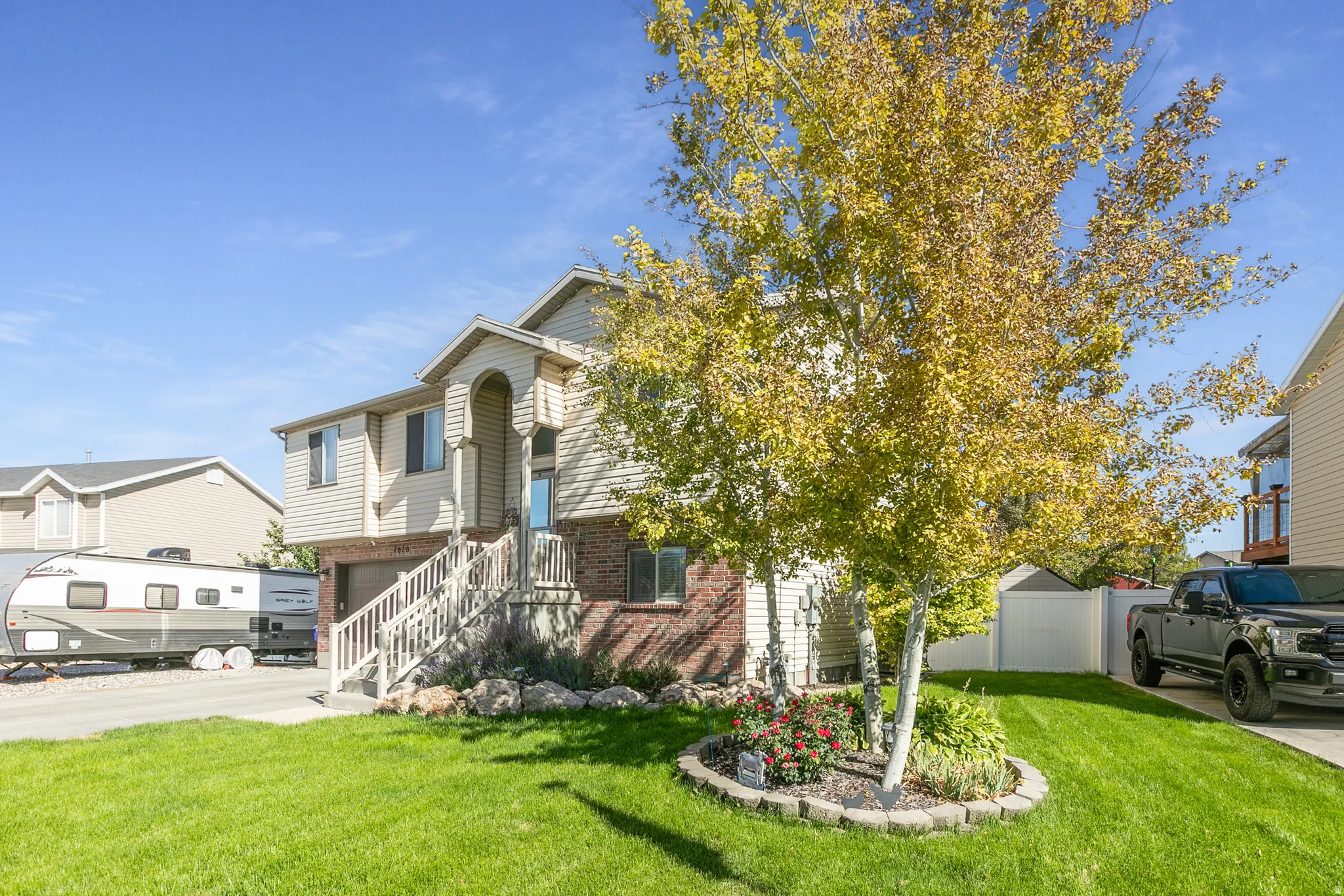 Two-story residence featuring a brick and siding exterior, a prominent front entrance with a covered porch, an attached garage, and a lush lawn with mature trees and landscaping