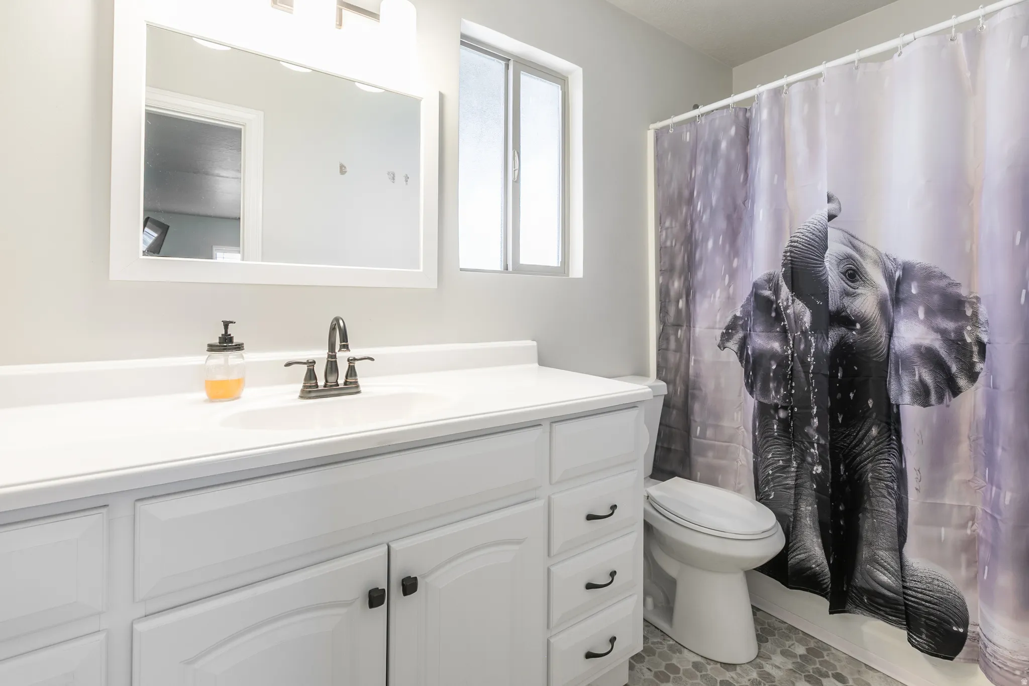 White vanity with integrated sink, dark bronze-finish faucet, framed mirror, and hexagonal floor tile