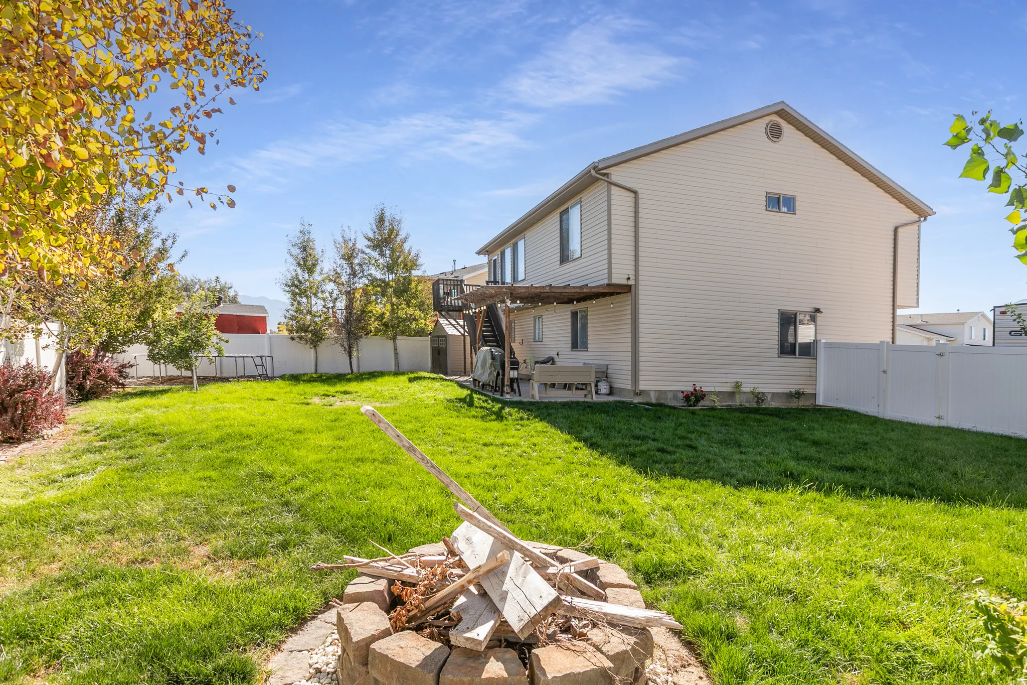 Expansive backyard featuring a stone-lined fire pit, manicured lawn, and a white privacy fence