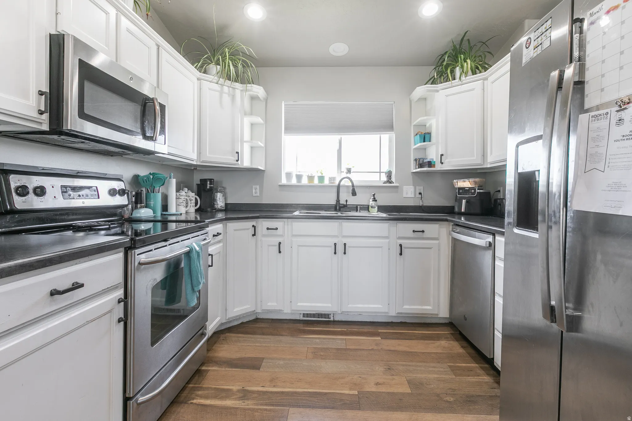 U-shaped kitchen featuring white cabinetry, dark countertops, wood-finish flooring, stainless steel appliances, and an undermount sink with a black faucet