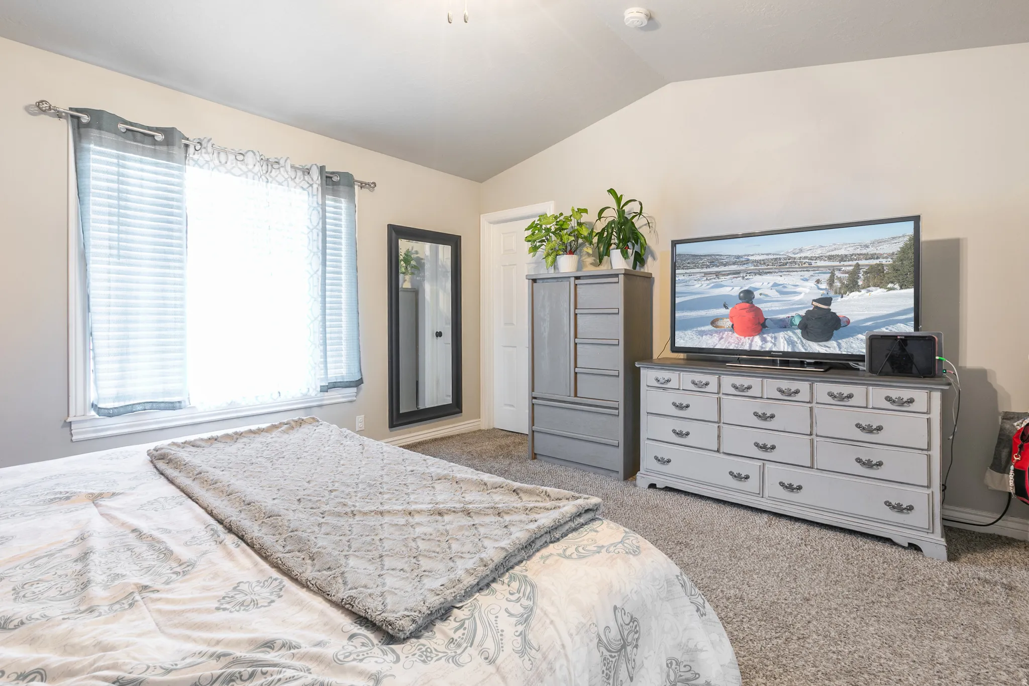 Vaulted ceiling, carpeted flooring, and a large window with blinds