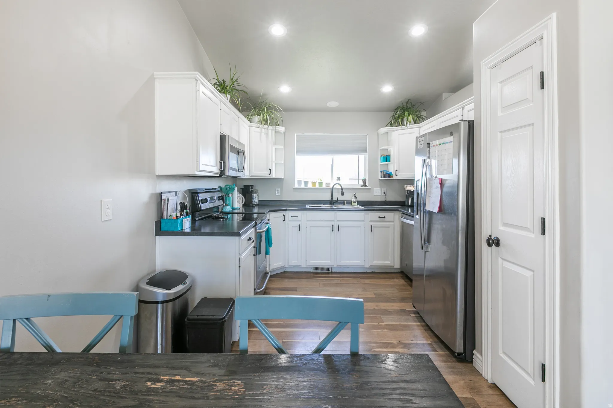 Kitchen featuring white cabinetry, dark countertops, stainless steel appliances, wood-finish flooring, and recessed lighting