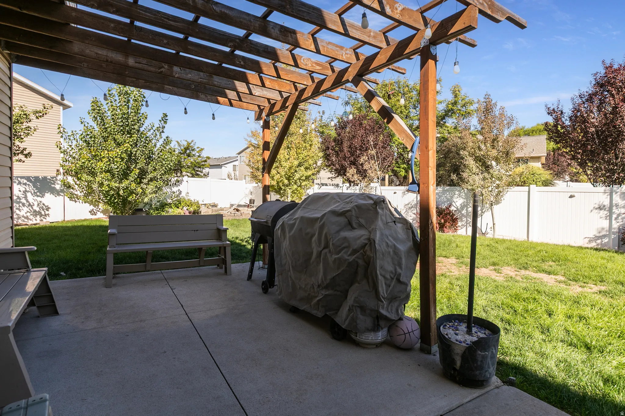Concrete patio with a wood pergola, string lighting, and direct access to a fenced yard with mature trees