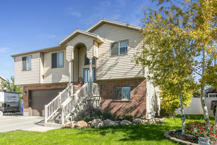 Split-level exterior featuring brick and siding, covered front entry, attached garage, and mature landscaping