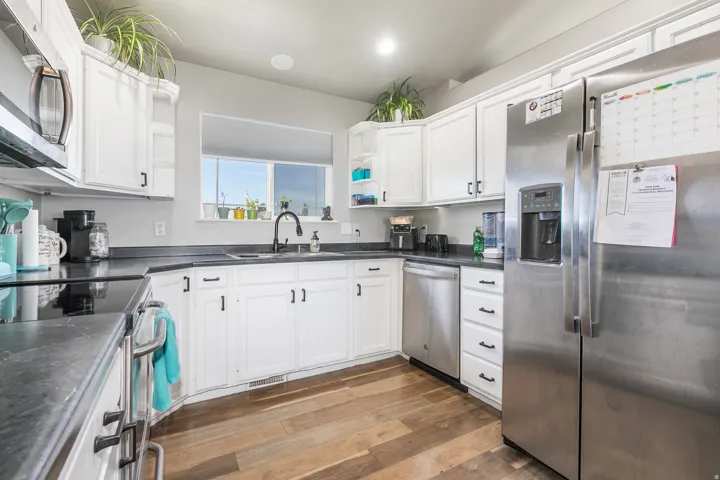 Kitchen featuring white cabinetry, dark countertops, wood-finish flooring, stainless steel appliances, and a window above the sink