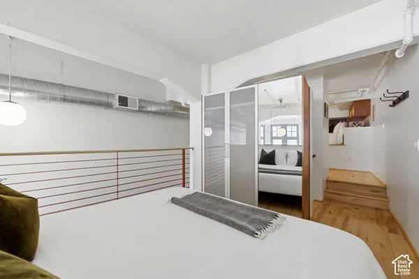 Loft bedroom featuring a wire railing, exposed ceiling ductwork, built-in storage closets with mirrored doors, and wood-finish flooring leading to stairs
