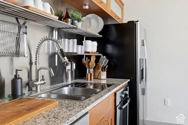 Kitchen featuring granite-style countertops, stainless steel appliances, a dual basin sink, a commercial-style faucet, and wood cabinetry