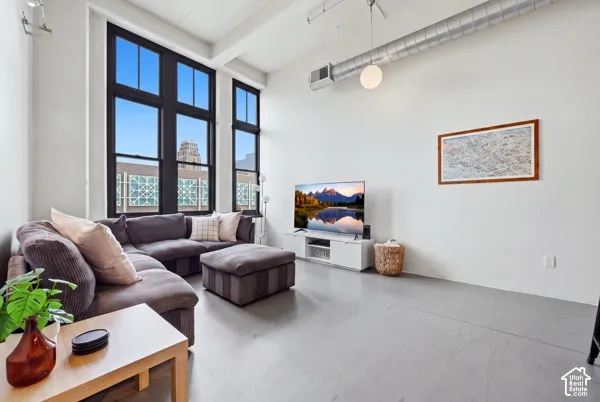Expansive windows with dark framing, exposed ceiling ductwork, high ceilings, pendant lighting, and light gray flooring