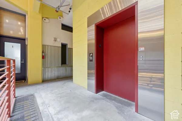 Elevator access with a red door and stainless steel frame, concrete flooring, and corrugated metal wall accents