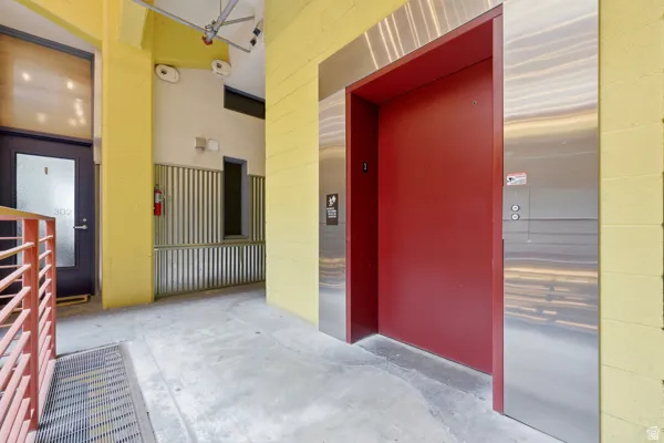 Elevator access with a red door and stainless steel frame, concrete flooring, and corrugated metal wall accents