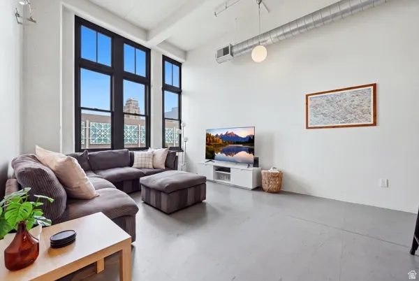 Expansive windows with dark framing, exposed ceiling ductwork, high ceilings, pendant lighting, and light gray flooring