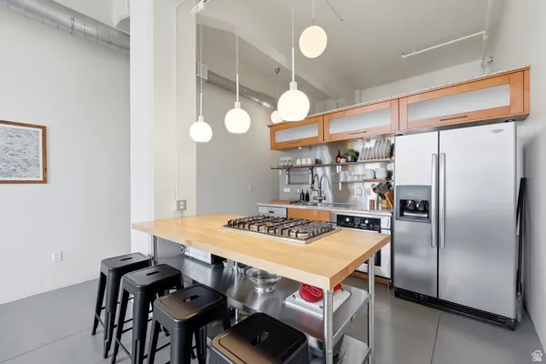 Kitchen featuring stainless steel appliances, wood-finish cabinetry with frosted glass inserts, a center island with a built-in gas cooktop, and suspended spherical light fixtures