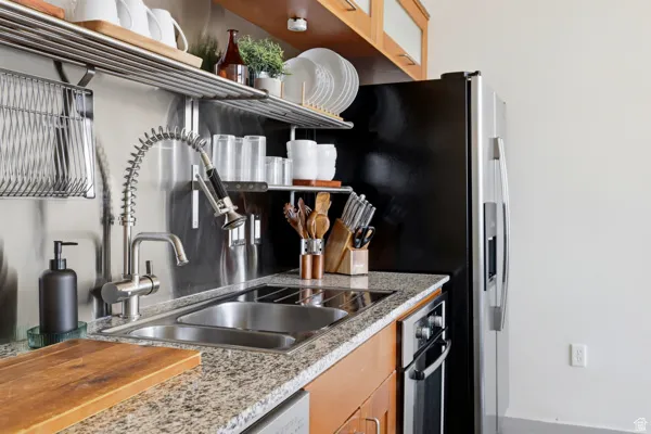 Kitchen featuring granite-style countertops, stainless steel appliances, a dual basin sink, a commercial-style faucet, and wood cabinetry