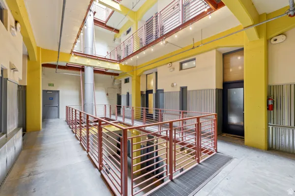 Multi-level interior corridor with concrete flooring, exposed structural beams, and industrial-style railings