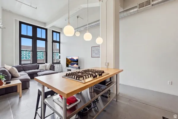 Open-concept living area featuring high ceilings, exposed ductwork, wood-finish flooring, a kitchen island with a gas cooktop, and tall multi-pane windows