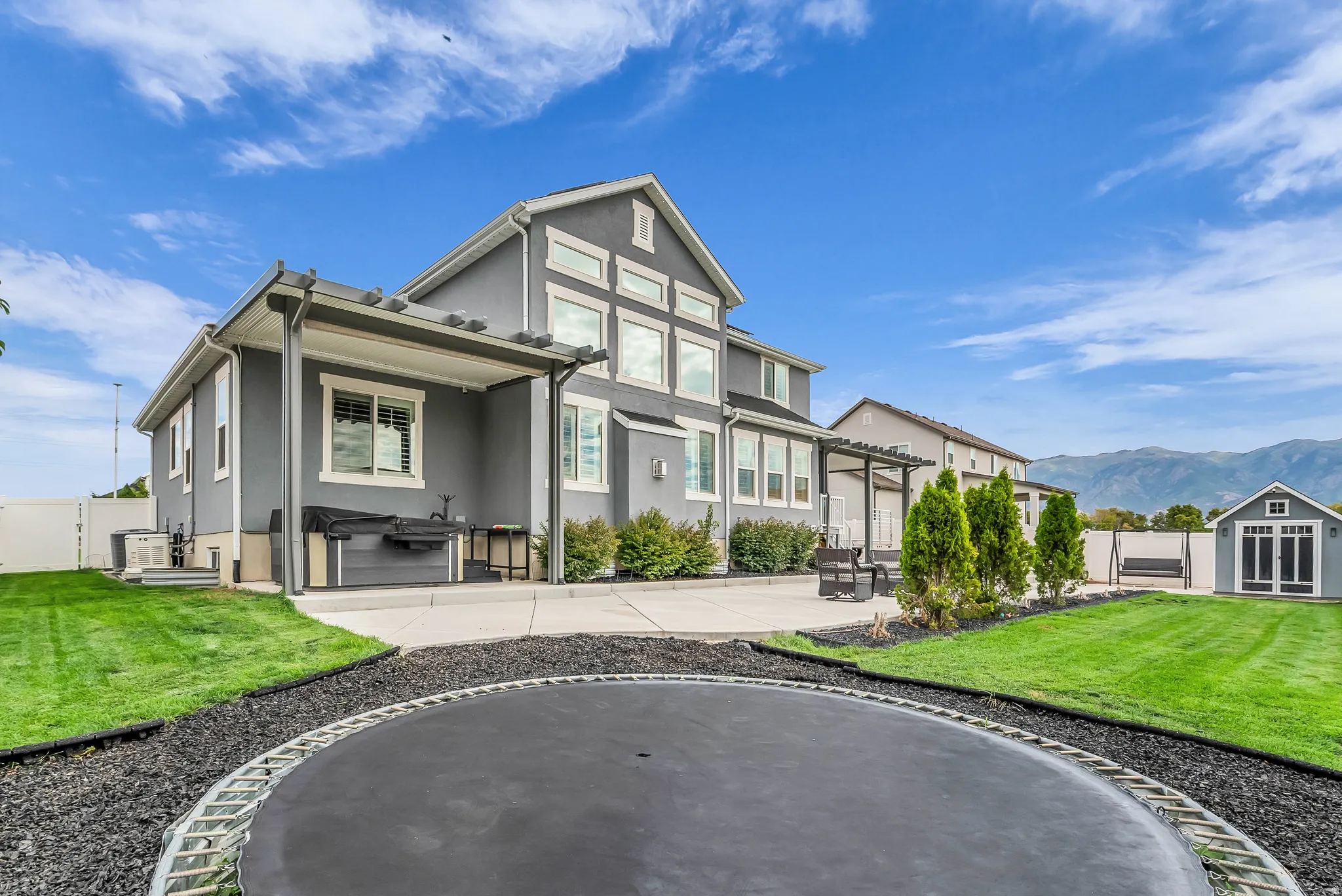Modern farmhouse exterior with board-and-batten siding and gabled roofline, featuring a covered front porch, multi-pane windows, and professional landscaping with manicured lawn, mature evergreen plantings, and decorative stone edging