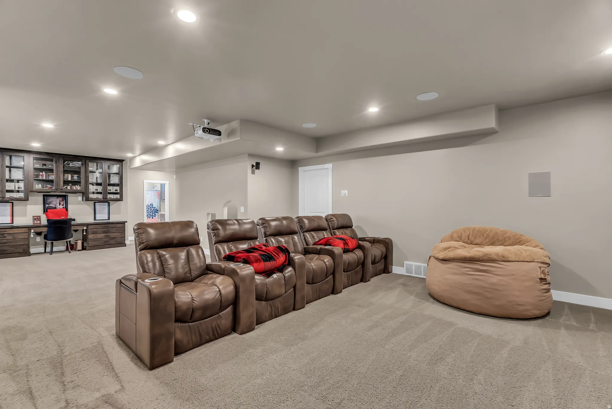 Recessed lighting illuminates a spacious room with light-toned carpeting and neutral wall paint