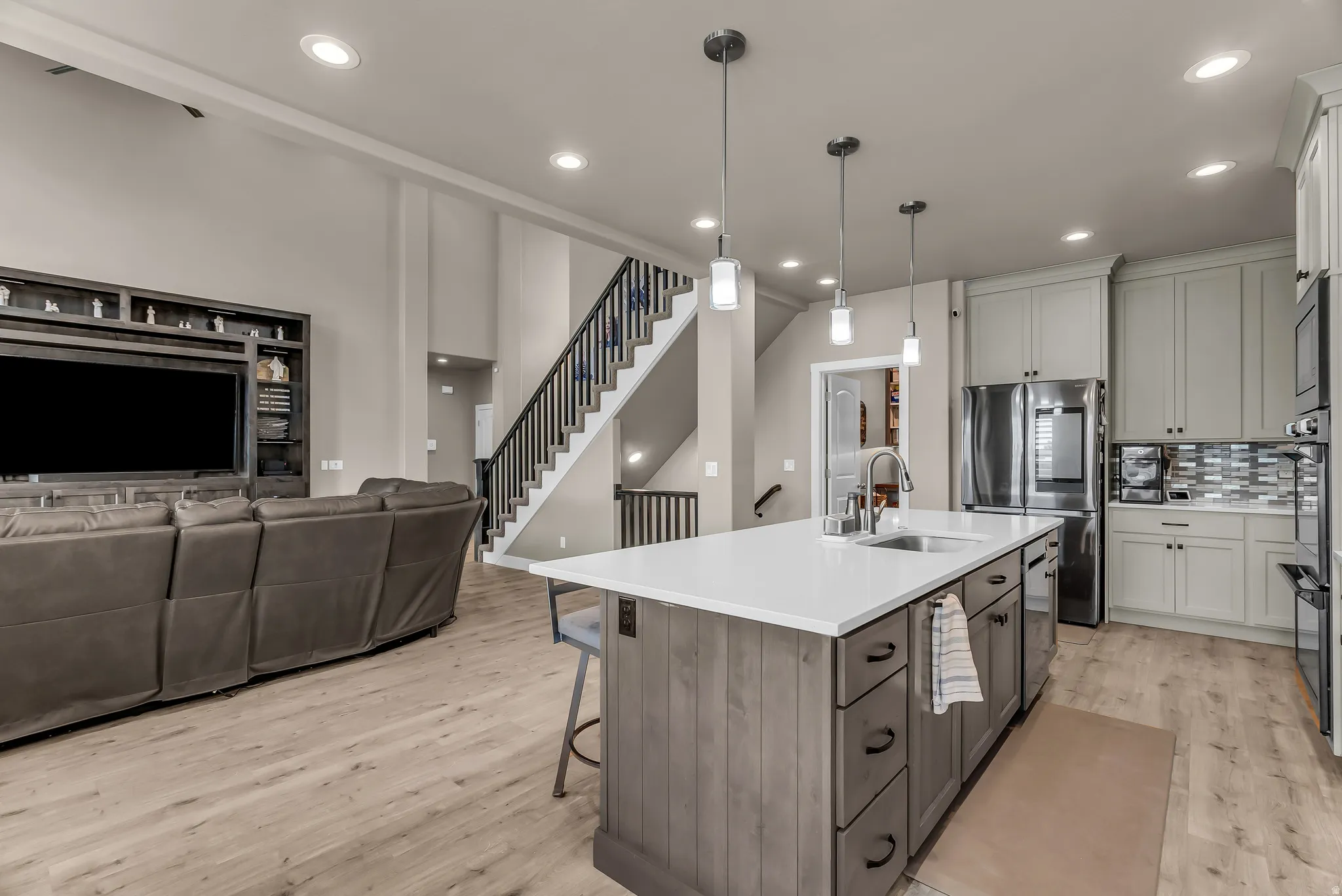 Open-concept living area with wood-finish flooring, a kitchen island featuring a sink, and pendant lighting
